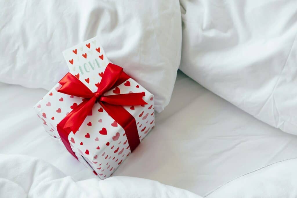 A box with a gift and a valentine card for a loved one lies on the bed